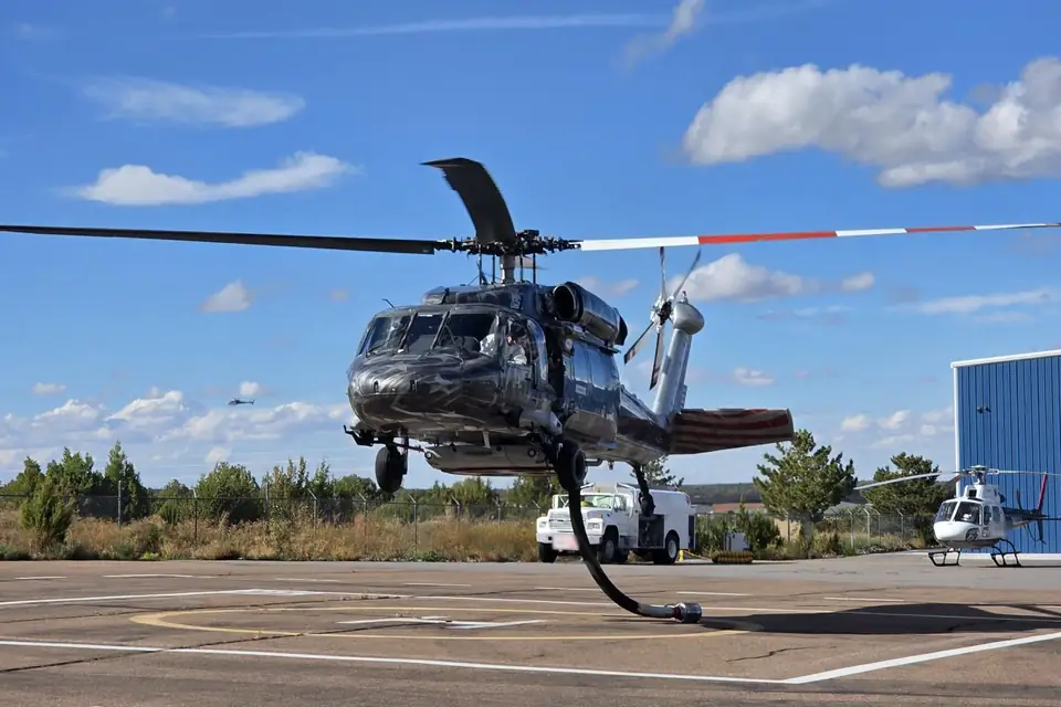 Castleberry UH-60 Black Hawk lifting off from a helipad under a blue sky, its red-and-white-tipped main rotor blades turning
