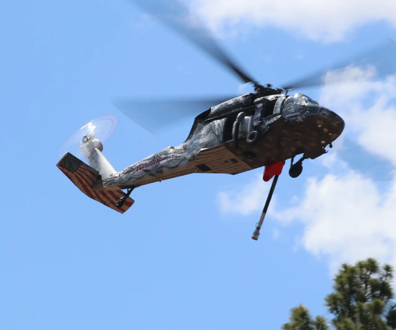 Castleberry UH-60 Black Hawk in flight over pine trees, in a custom star livery with a flag-painted tail and a water snorkel hanging below