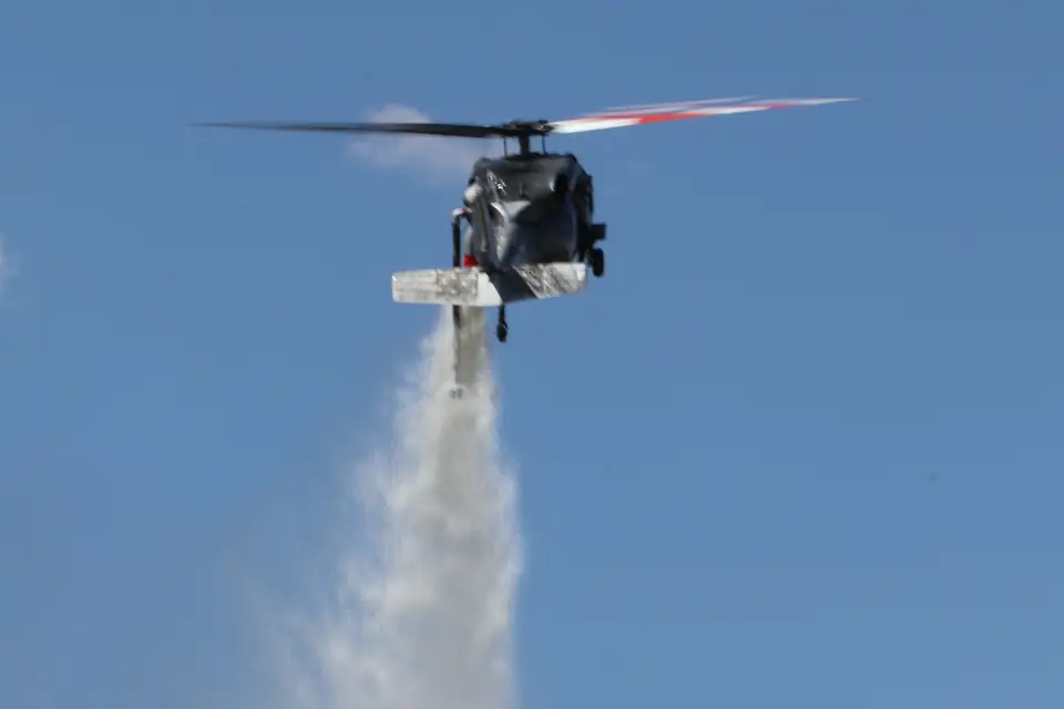 Castleberry Black Hawk releasing a water drop against a blue sky, its red-and-white-tipped rotor blades turning