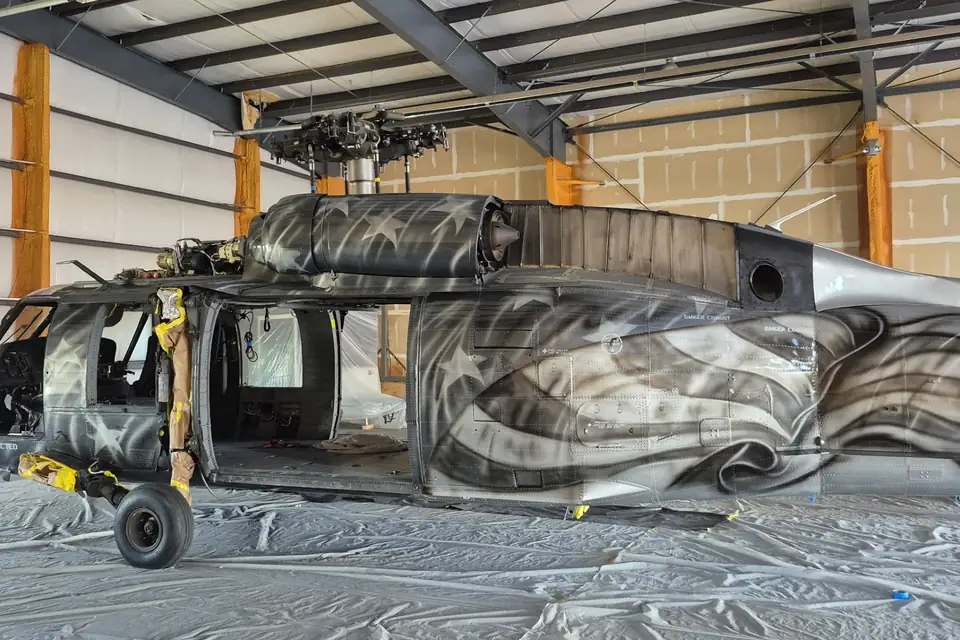 UH-60 Black Hawk in the CAS paint hangar, a custom flag-and-eagle livery in progress along its tail section and stars on the engine cowling