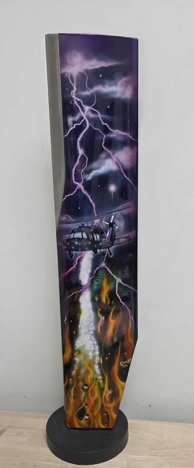 Painted rotor blade art piece on a display base: a Black Hawk in purple lightning, dropping water on a forest fire