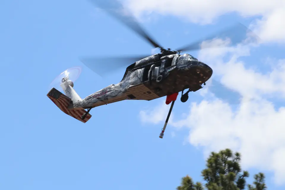 Castleberry UH-60 Black Hawk in flight over pine trees, in a custom star livery with a flag-painted tail and a water snorkel hanging below