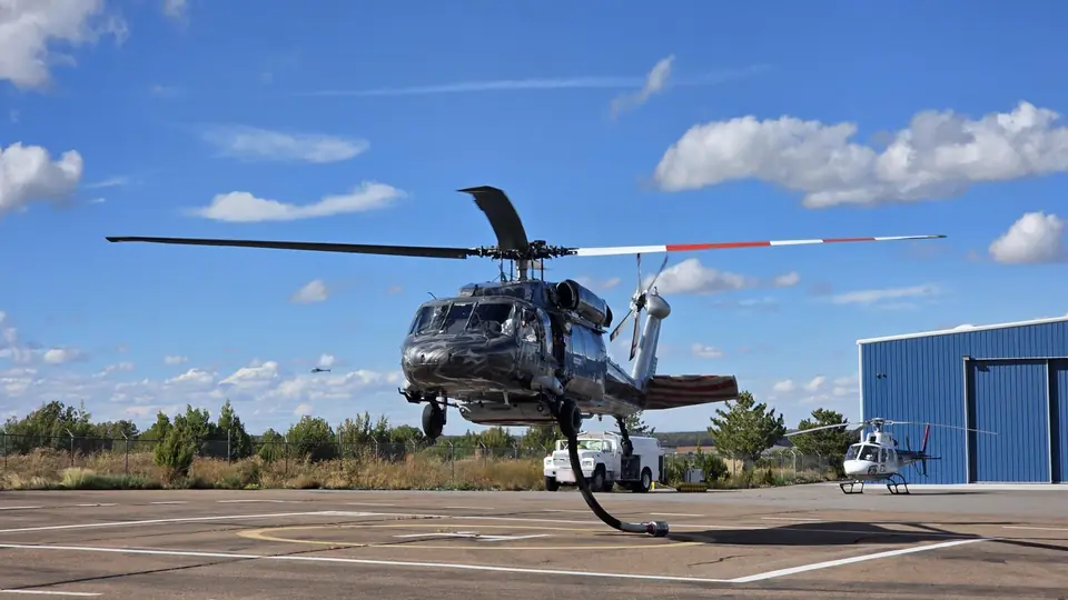 Castleberry UH-60 Black Hawk in a custom flag livery lifting off a helipad beside a blue hangar