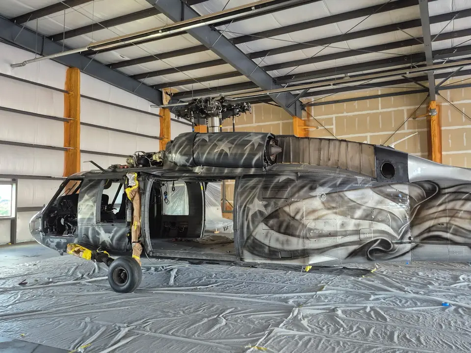 UH-60 Black Hawk in the CAS paint hangar, with a custom flag-and-eagle livery in progress and the floor under plastic sheeting