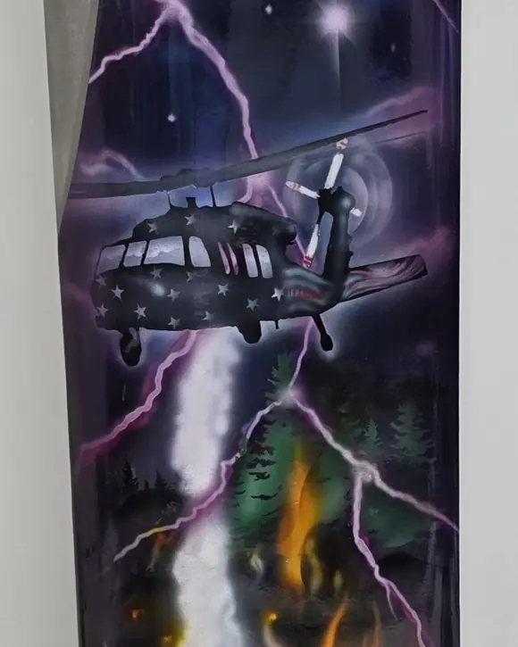 Detail of a painted rotor blade: a Black Hawk with stars on its fuselage flies through purple lightning above a forest fire