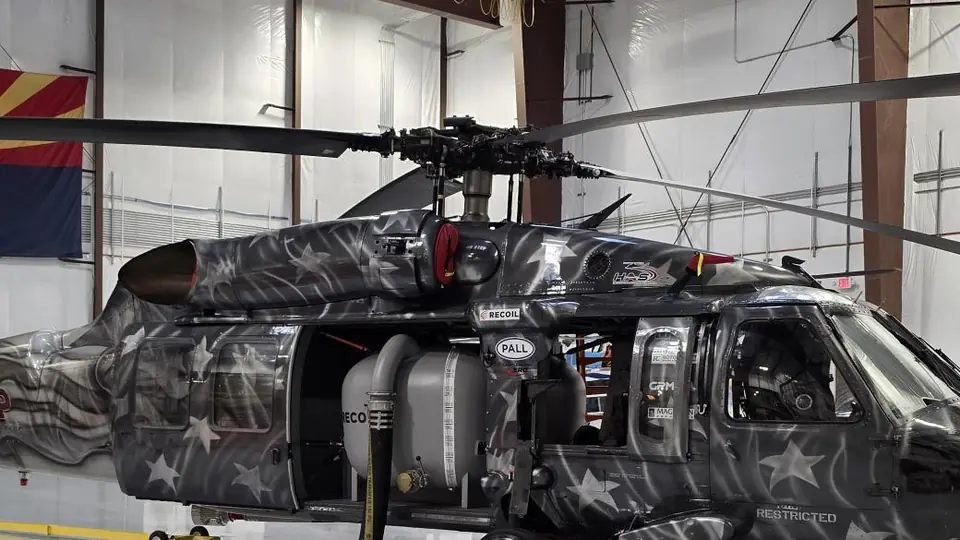 The main rotor head and blades above the engine cowling of a UH-60 Black Hawk in a star livery, in a hangar