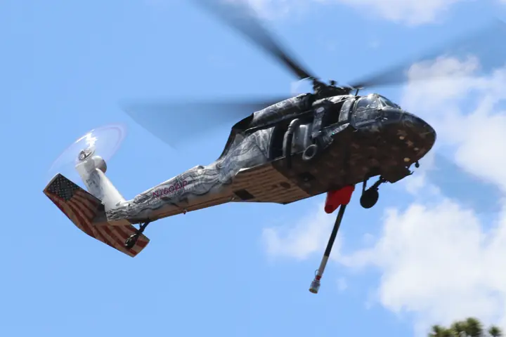 Castleberry UH-60 Black Hawk in flight over pine trees, in its star livery with a flag-painted tail