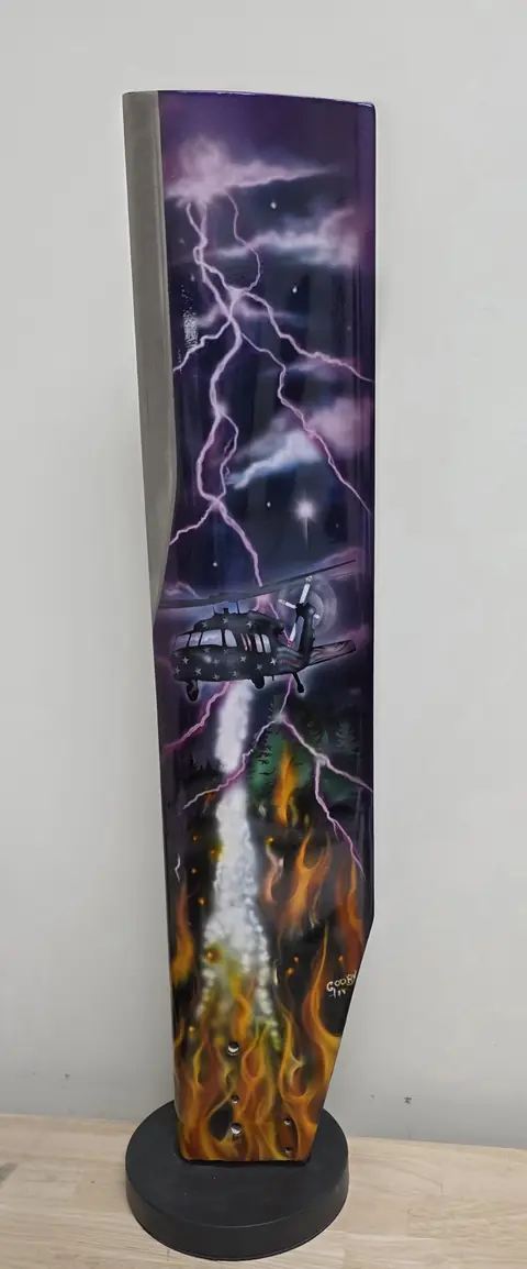 Painted rotor blade art piece on a display base: a Black Hawk in purple lightning, dropping water on a forest fire